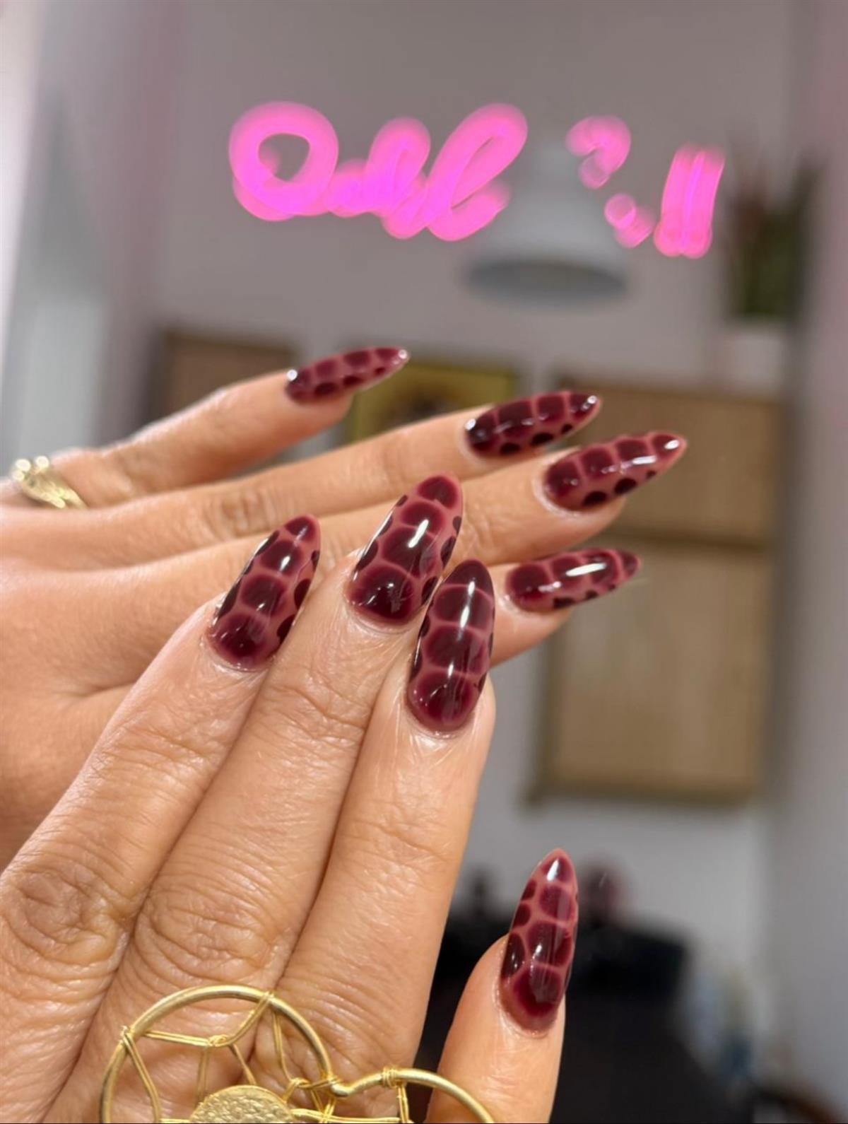 Uñas bordeaux con diseño de cuadros frente al letrero de neón Ooh la la del estudio